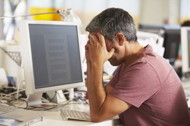 Stressed Man Working At Desk In Busy Creative Office