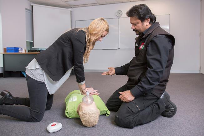 First aid trainer showing a woman how to do CPR compressions