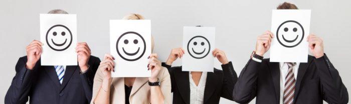 4 office workers holding a happy smiley face piece of paper in front of their faces