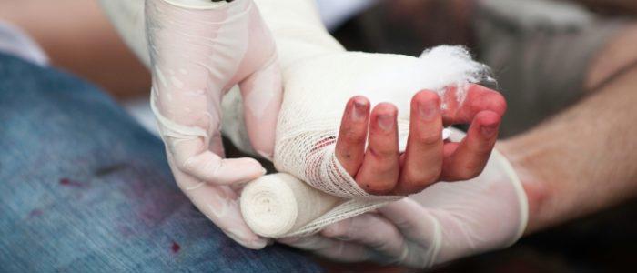 gloved first aider bandaging an injured hand with gauze bandage