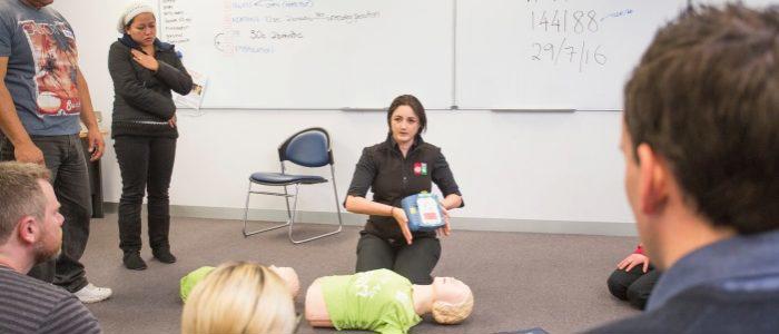 St John trainer with defibrillator showing training class how to use it