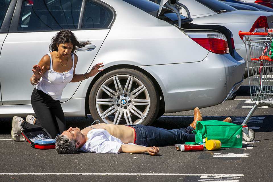 woman using a defibrillator on a man in a car park